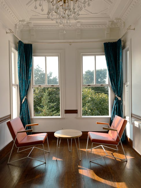 Modern sitting area with two chairs, a table, and sunlight streaming through windows.